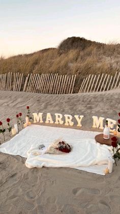 a sign that says marry me on the beach with flowers and candles in front of it