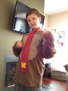 a young boy dressed up as a man with a tie and bear costume on standing in front of a flat screen tv