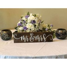 a wooden sign sitting on top of a table next to two vases filled with flowers