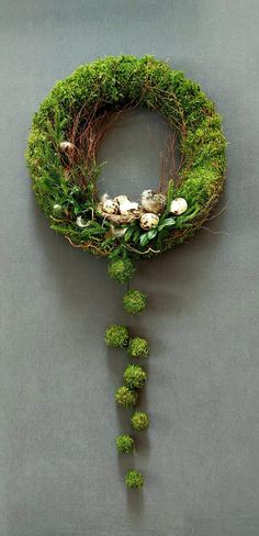 a green wreath with white flowers and moss hanging from it's side on a gray wall