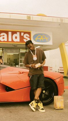 a man sitting on the hood of a sports car in front of a store with his cell phone