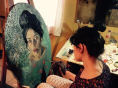 a woman sitting in front of a painting on a easel