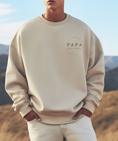 a man standing in the grass with his hands on his hips wearing a sweatshirt that says papa