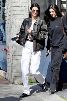 two women are walking down the street in white pants and black jacket, one is wearing sunglasses