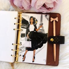 an open notebook with a fashion illustration on it and a pink flower next to it