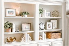 a white book shelf filled with lots of books and pictures next to a clock on top of it