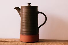 a brown and black ceramic tea pot sitting on top of a wooden table next to a white wall