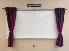 a white board mounted to the side of a wall next to red curtained windows