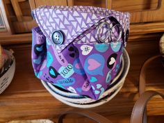 a purple purse sitting on top of a wooden table next to a basket with scissors in it