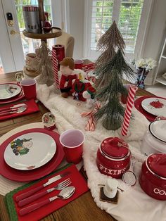 the table is set for christmas with red and white dishes, silverware, and candy canes