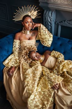 two women in gold dresses sitting on a blue couch with their arms around each other