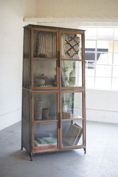 a tall metal and glass display case in an empty room with the door open to reveal books