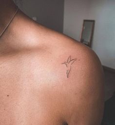 the back of a woman's shoulder with a small bird tattoo on it