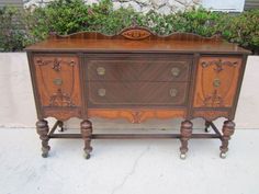 an old fashioned dresser is sitting outside on the sidewalk with potted plants behind it