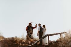 a man and woman standing on top of a rocky hill next to a wooden rail