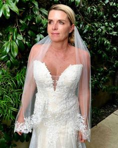 a woman wearing a wedding dress and veil standing in front of a bush with greenery