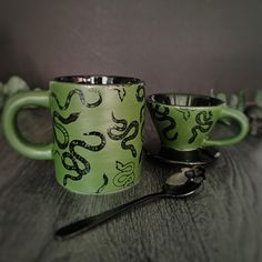 two green coffee mugs sitting next to each other on a wooden table with spoons