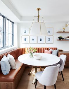 a dining room table with four chairs and a bench in front of the window that has pictures on the wall above it