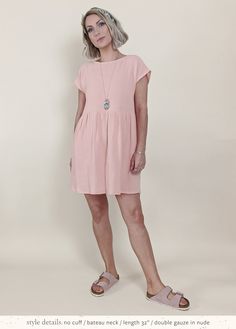 a woman standing in front of a white wall wearing sandals and a pink shirt dress