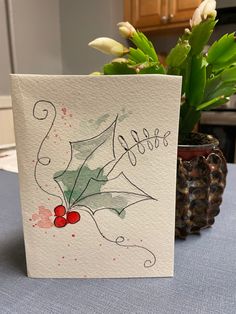 a greeting card with holly berries and the word love written on it next to a potted plant