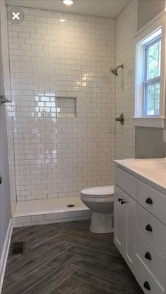 a white bathroom with wood flooring and tiled shower stall, toilet and sink area