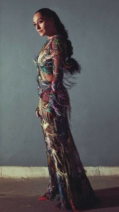 a woman in a long dress with feathers on her head and hands behind her back