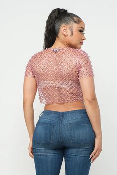 a woman wearing jeans and a pink top with sequins on the shoulders, back view