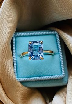 an engagement ring with a blue topazte in a velvet box on a beige cloth