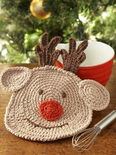 a crocheted reindeer hat and whisk on a table next to a christmas tree