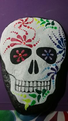 a rock with a painted skull on it sitting next to a purple wall and colorful flowers