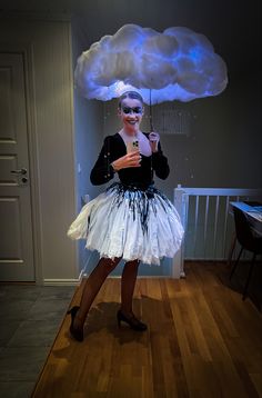 a woman in a tutu and mask holding an umbrella under a cloud shaped object