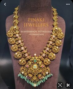 a gold necklace with green and pink stones on display in front of a mannequin