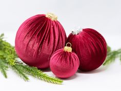 two red christmas ornaments sitting next to each other on a white surface with greenery