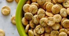 a green bowl filled with crackers on top of a white countertop next to other small pieces of food