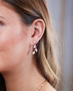 a close up of a woman's ear wearing gold and white earrings with flowers on them