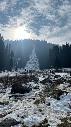 the sun shines brightly over a snow covered mountain stream with rocks and trees in the foreground