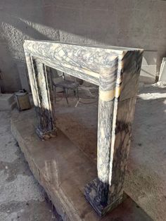 an old marble fireplace surround in the middle of a concrete area with chairs and tables around it