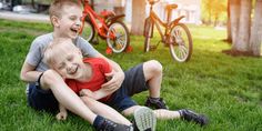 two young boys sitting on the grass with their arms around each other and one boy holding his head