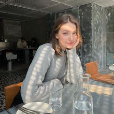 a woman sitting at a table in front of a glass vase with water on it