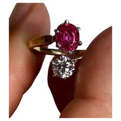 a woman's hand holding an engagement ring with a pink diamond