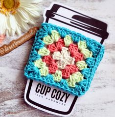 a small crochet square is sitting next to a flower