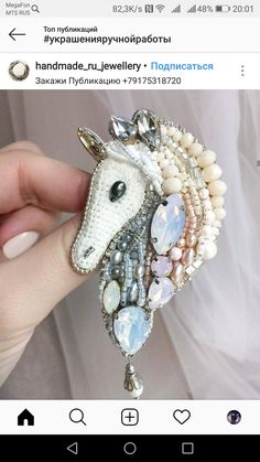 a hand holding a horse brooch with pearls and jewels on it's head