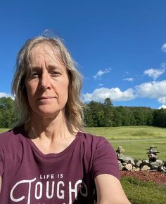 a woman in a purple shirt holding a frisbee with her right hand and looking at the camera