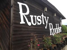 a wooden building with the words rusty riddle painted on it's side and flowers growing outside