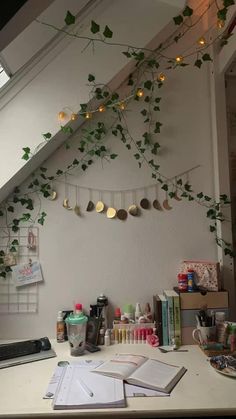 a cluttered desk under a slanted ceiling with ivy growing on the wall and hanging from it