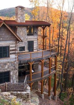 a stone and wood house surrounded by trees with fall foliage on the hillside in the background