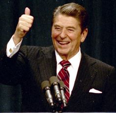 a man giving a thumbs up while standing in front of microphones with his hand raised