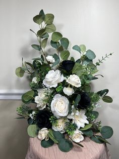 a bouquet of white and black flowers sitting on top of a pink tablecloth covered table