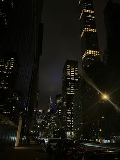 the city skyline is lit up at night with skyscrapers in the foreground and cars parked on the street