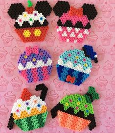 four different colored cupcakes made out of perler beads on a pink background